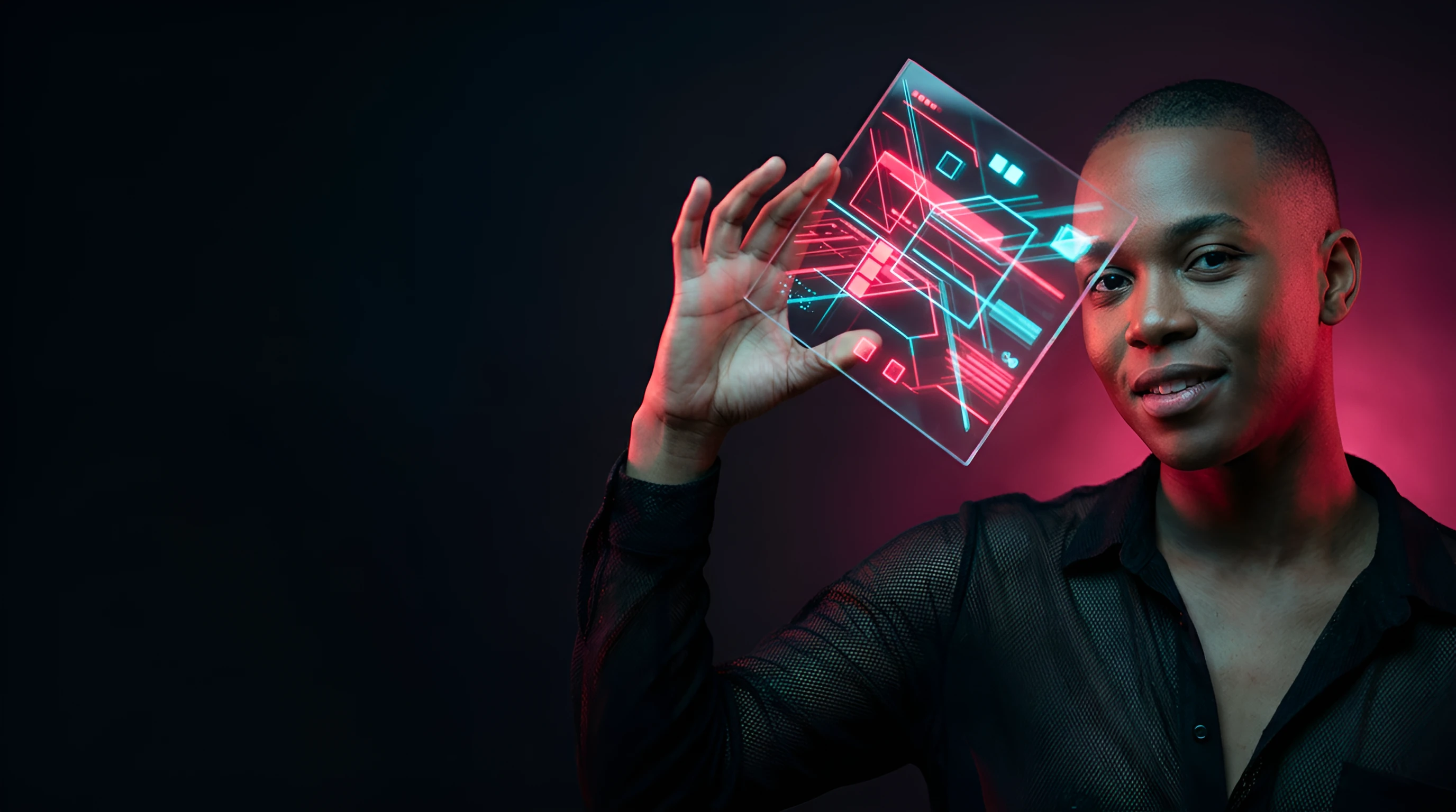 Smiling man in a black shirt holding up a translucent glass panel of pink and cyan circuit lines under magenta light