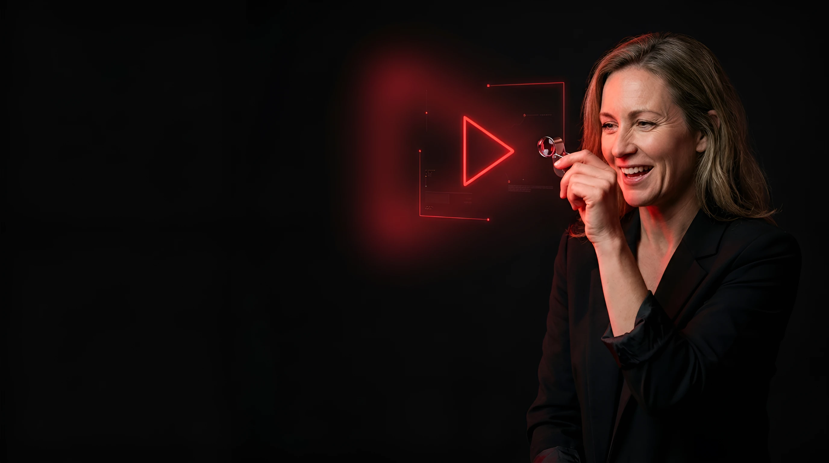 Smiling woman in a dark blazer holding a tiny camera lens beside a glowing red play-button outline